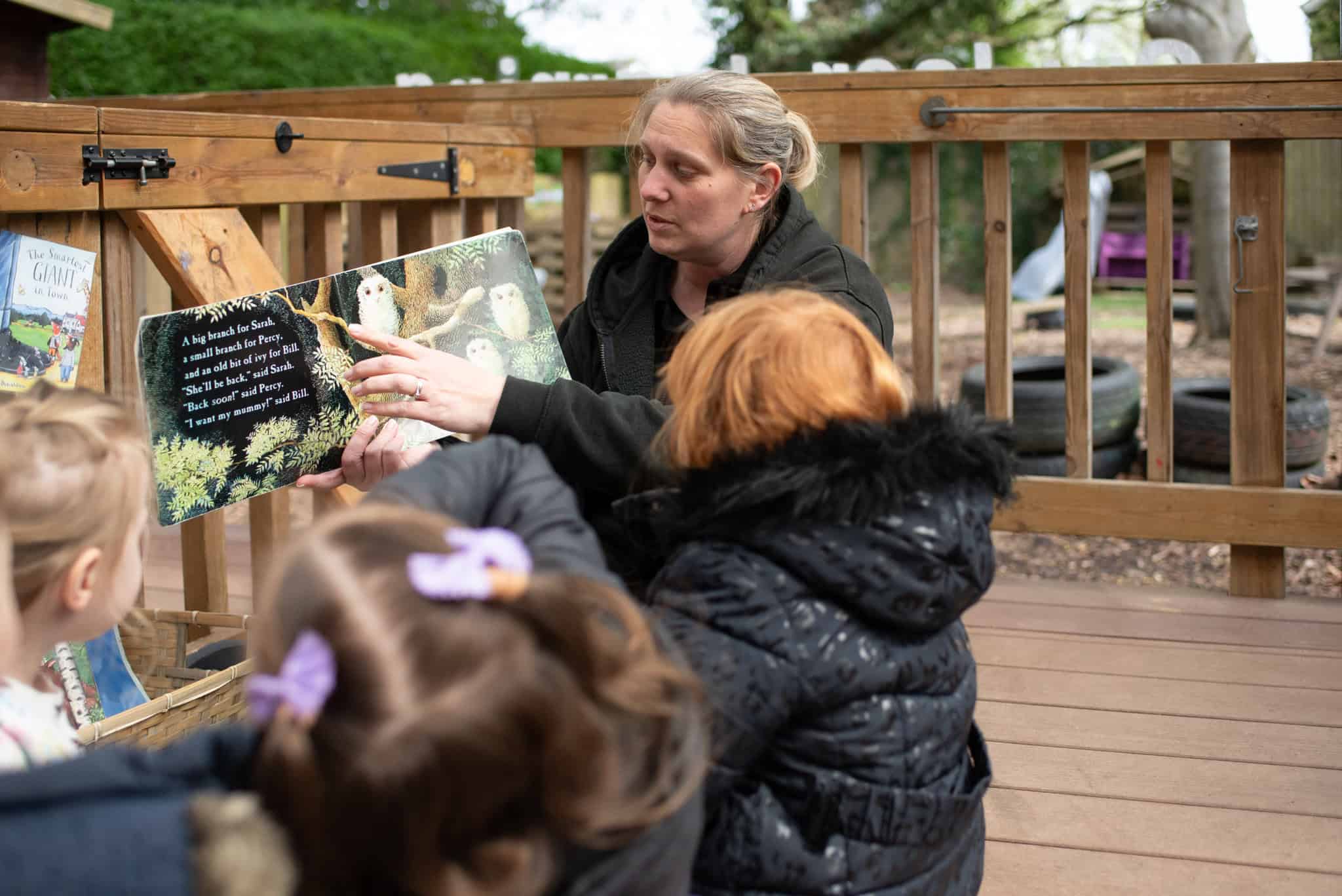 1. Educator reading a colourful children's book to preschool kids outdoors at Thrive Childcare in a garden setting.