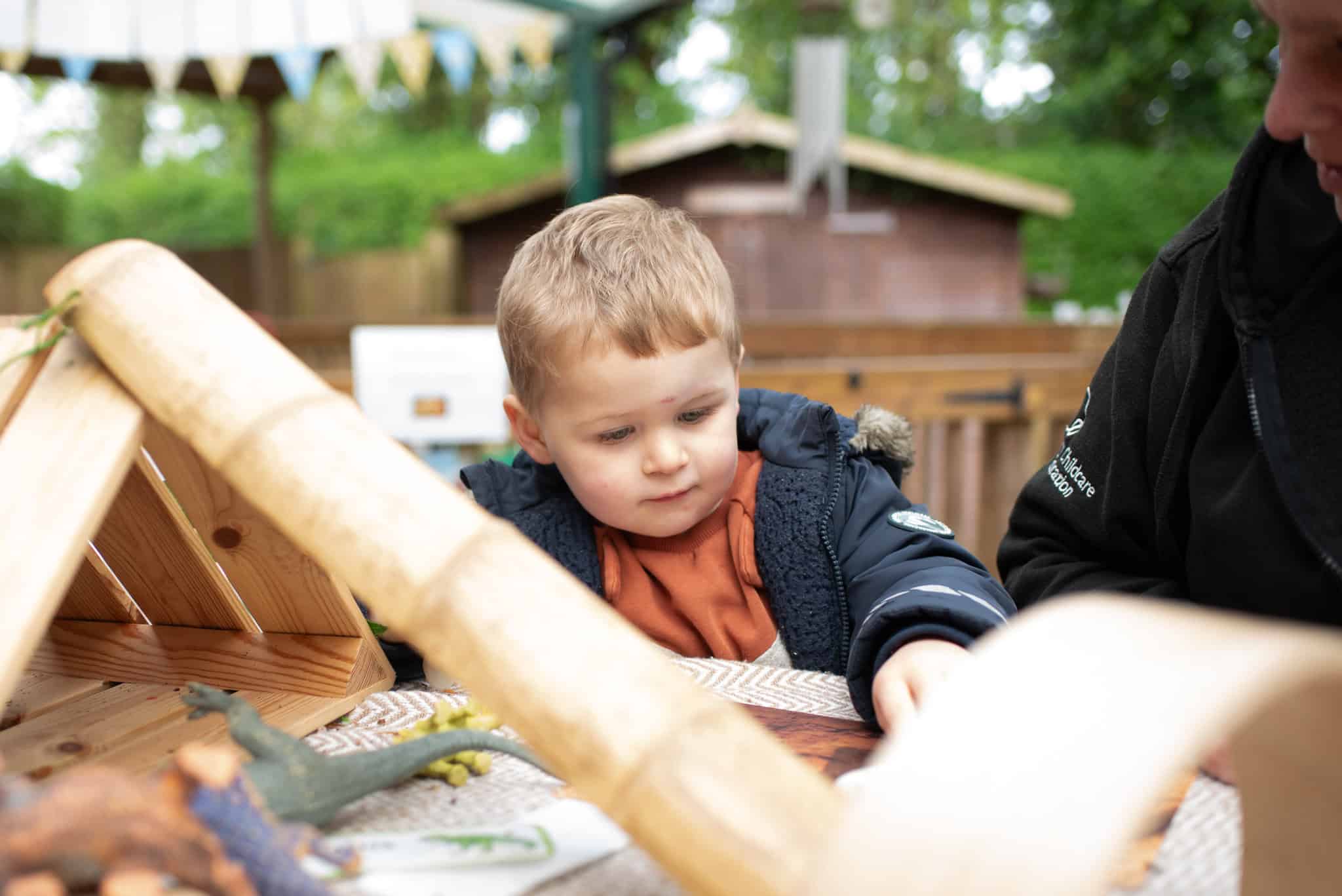 Young boy engaging in outdoor dinosaur-themed learning activity at Thrive Childcare, exploring toys and educational play in a natural childcare environment in the UK.