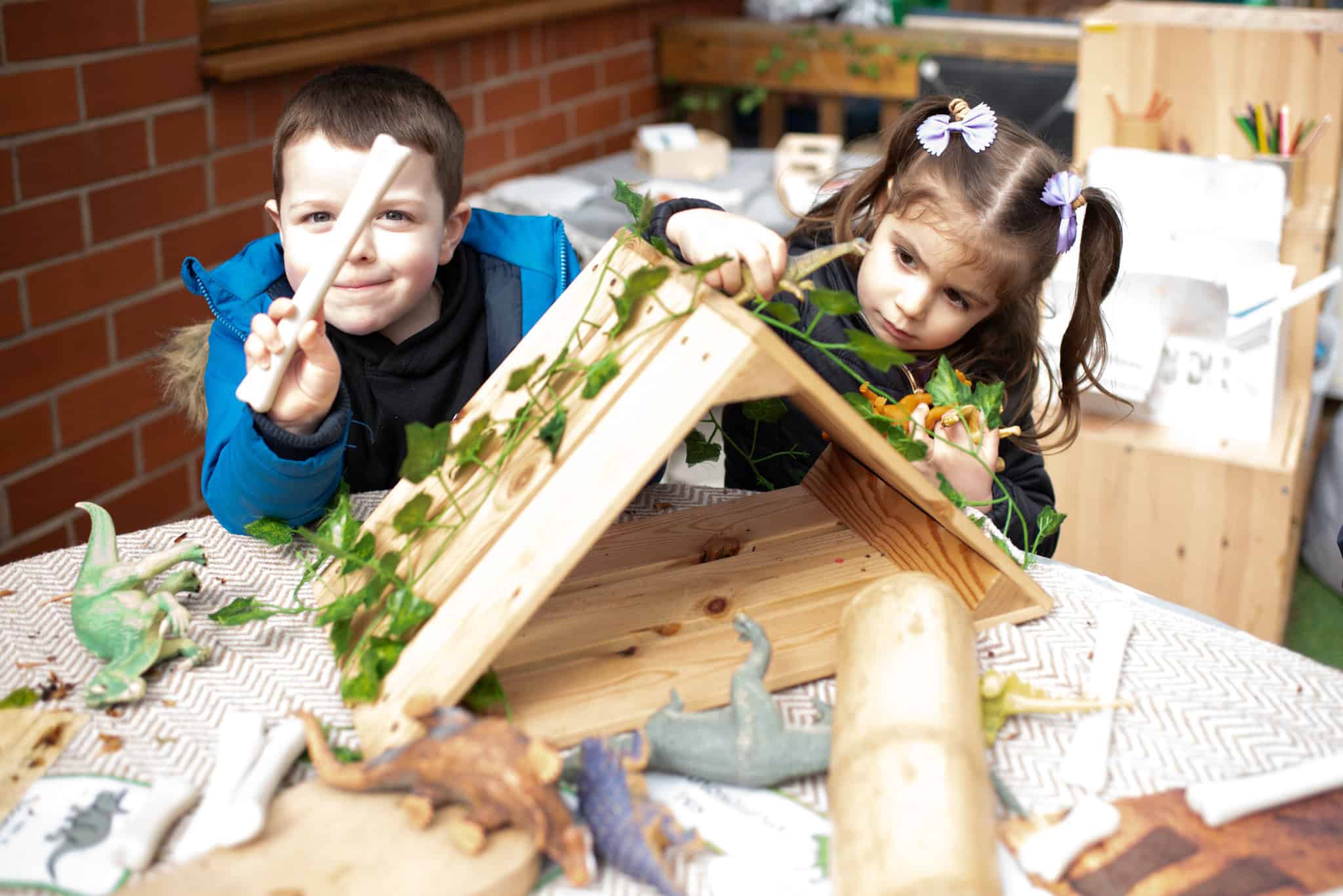 Bright young children engaging in outdoor creative play at Thrive Childcare, exploring nature with toys and natural materials in a safe, nurturing environment promoting early childhood development.