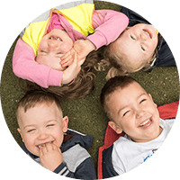 Bright happy children lying on the grass enjoying outdoor play at Thrive Childcare, promoting early childhood development in a safe and nurturing environment.