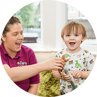 A caring childcare professional engaging with smiling toddler in a bright, safe nursery environment at Thrive Childcare, fostering early development and learning.