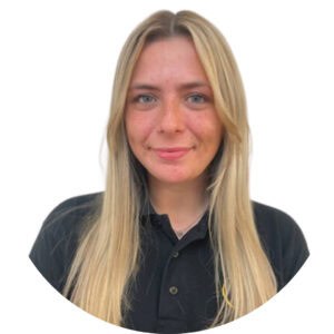 Caring childcare professional with blonde hair, wearing a black polo shirt, smiling warmly, representing Thrive Childcare’s dedicated team committed to child development and early education.