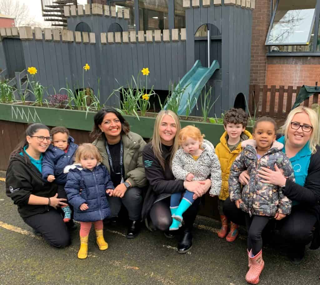 1. A group of diverse children with caregivers at Thrive Childcare outdoor play area, showcasing caring environment and outdoor activities for early childhood development.