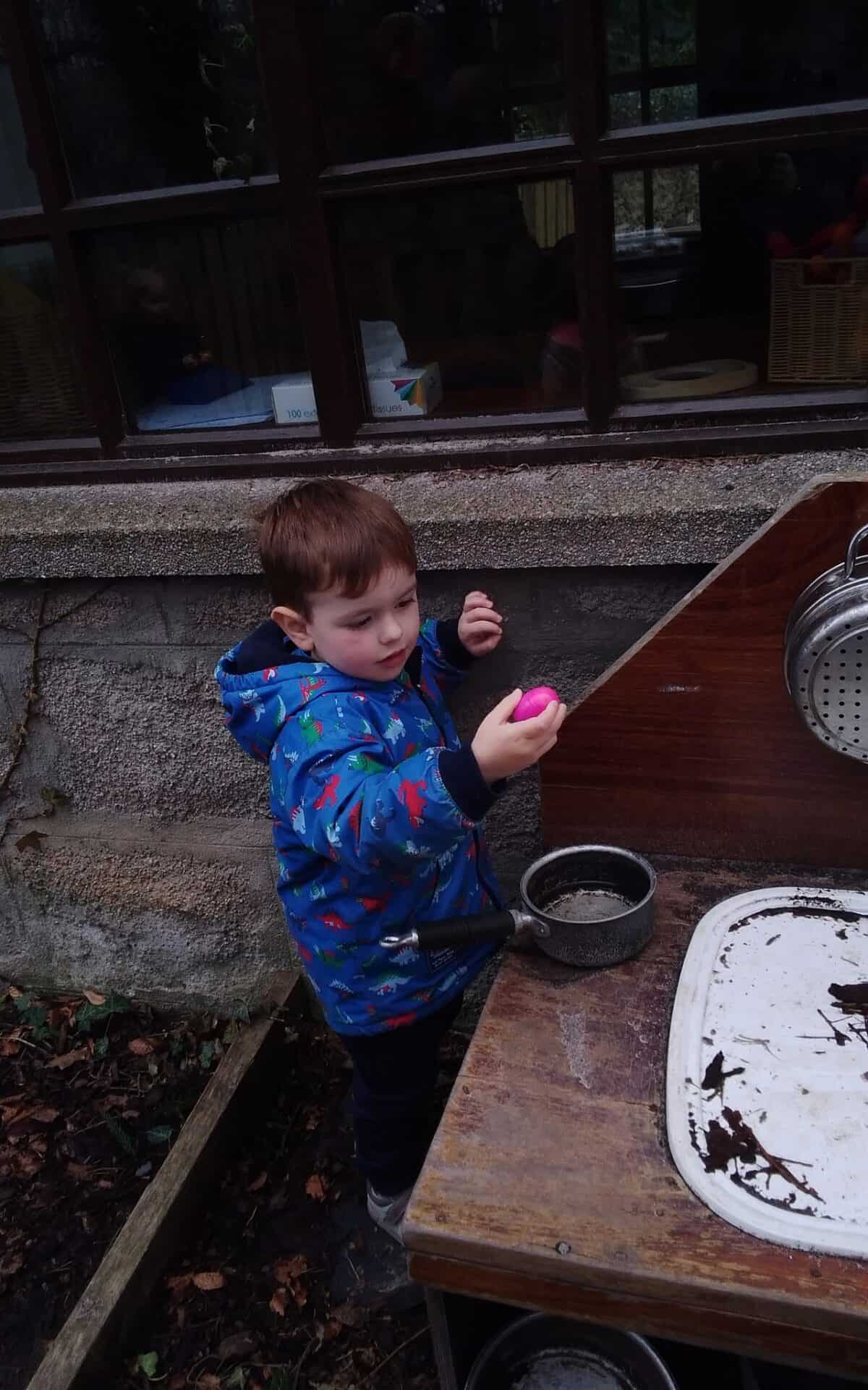 1. Young boy playing outdoors at Thrive Childcare, holding a pink egg in a safe, engaging environment designed for learning and development.