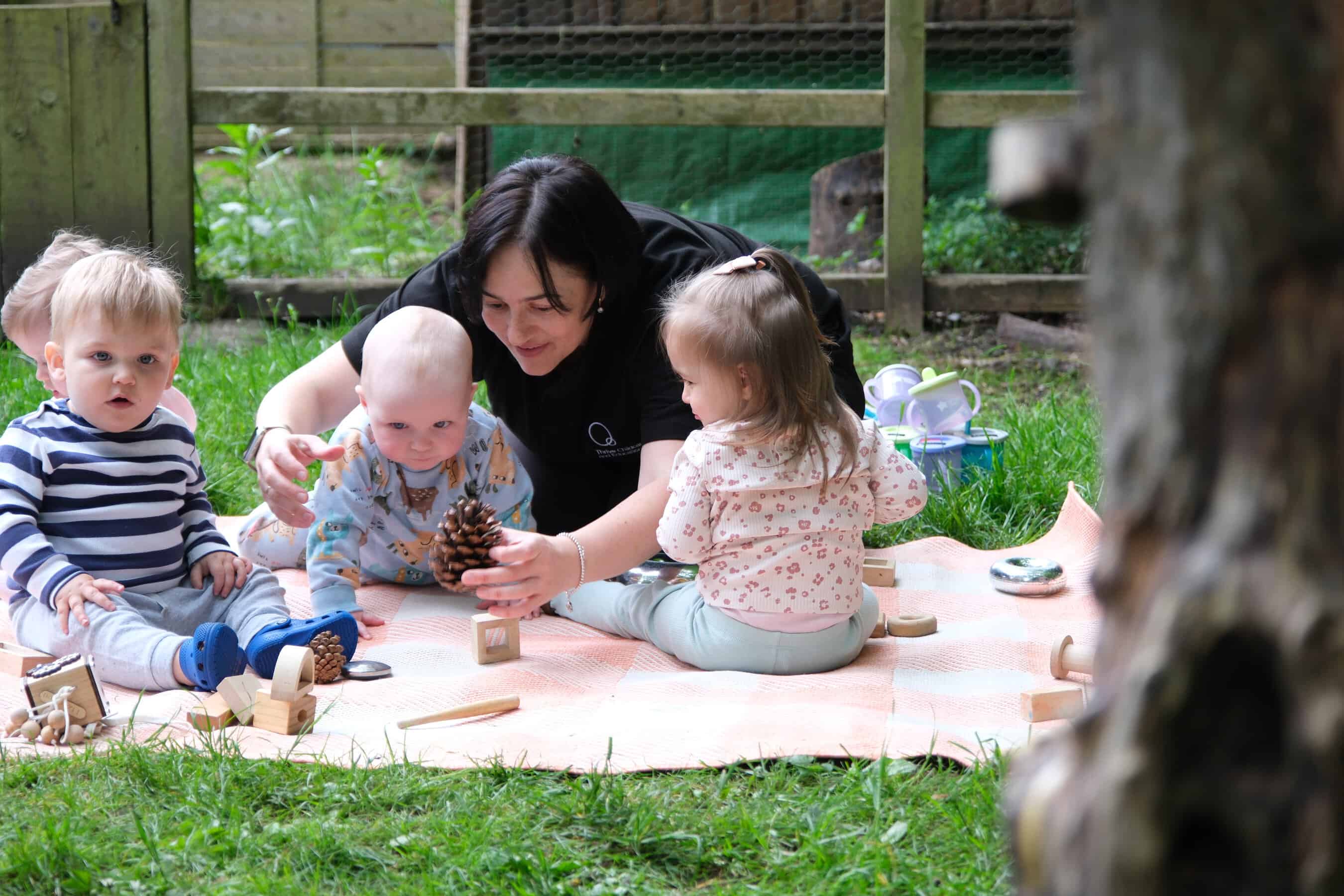 A babysitter playing with young children outdoors at Thrive Childcare, engaging them with natural toys and activities in a safe, nurturing environment.