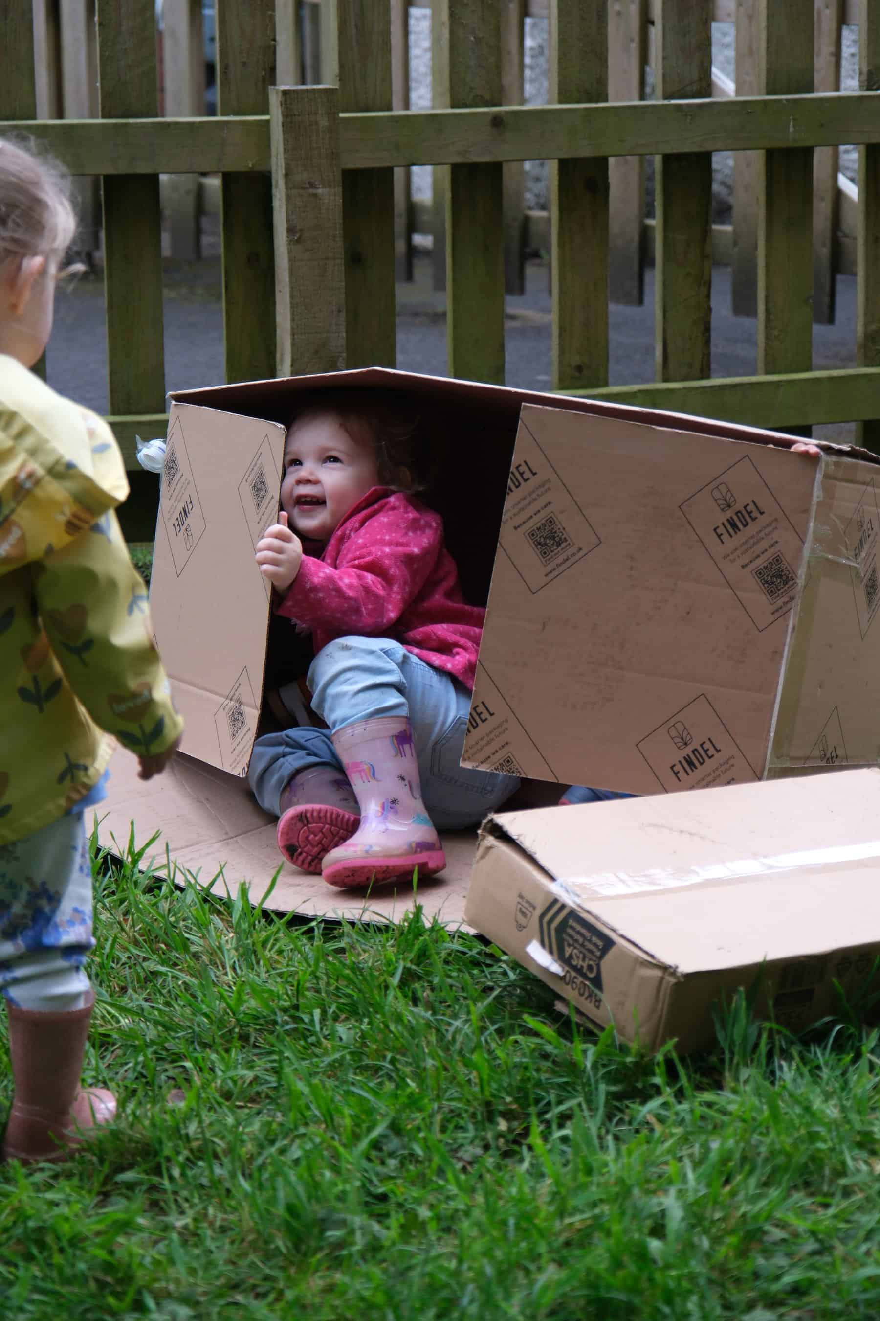 Excited young children playing in a cardboard box fort outdoors at Thrive Childcare, promoting creativity and outdoor fun for early childhood development.