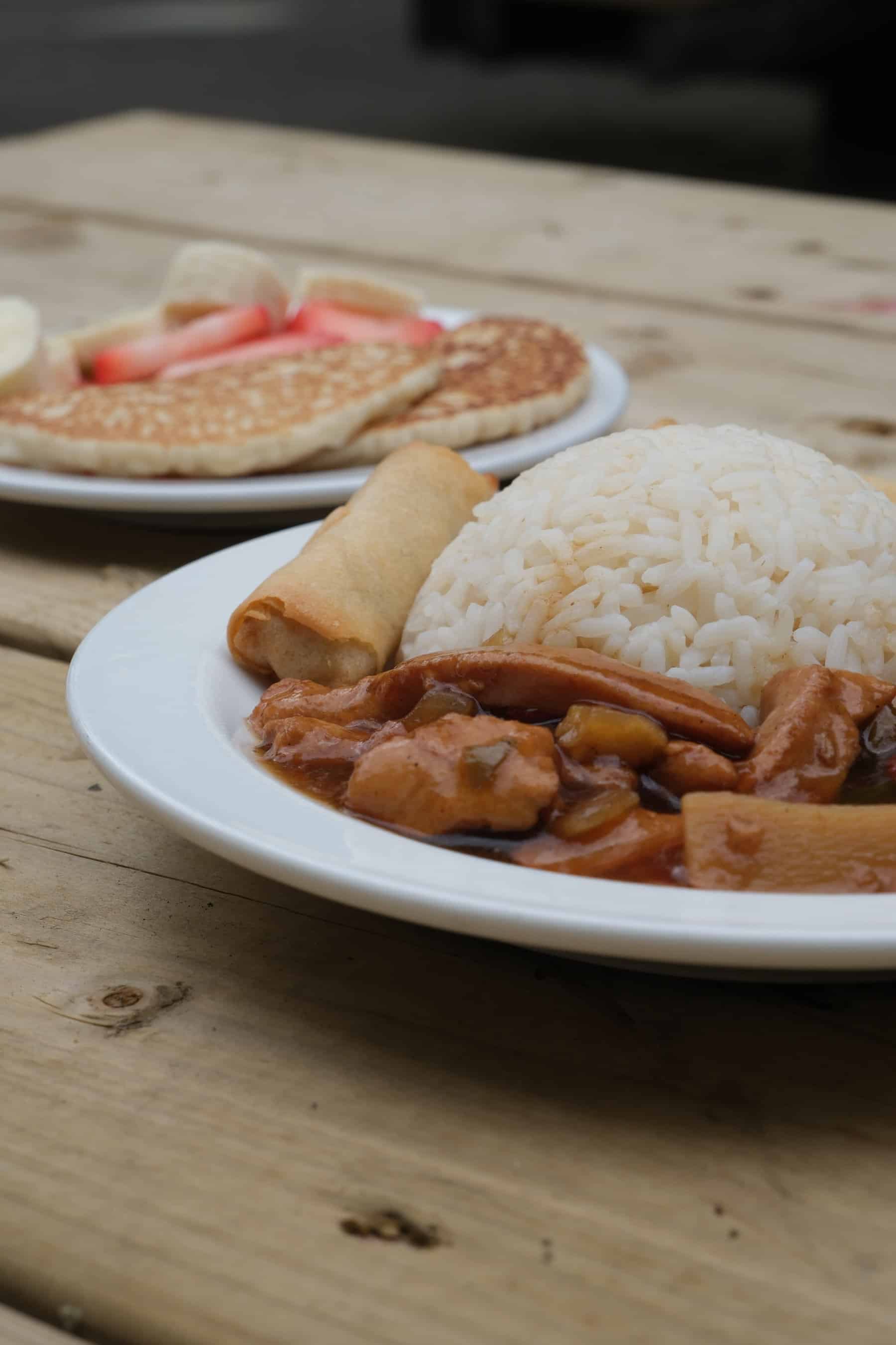 A colourful plate of rice, chicken stew, spring roll and a cozy breakfast of pancakes with fruit, served outdoors to children at Thrive Childcare, a trusted early years education provider.