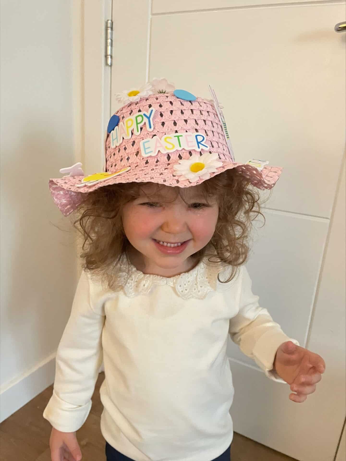 Bright young girl wearing a pink 'Happy Easter' decorated hat, enjoying festive celebrations at Thrive Childcare in a warm and welcoming environment.