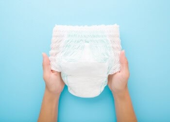 Soft disposable diaper held by hands against blue background, child care product for babies, Hygiene, comfort, and safety for young children.