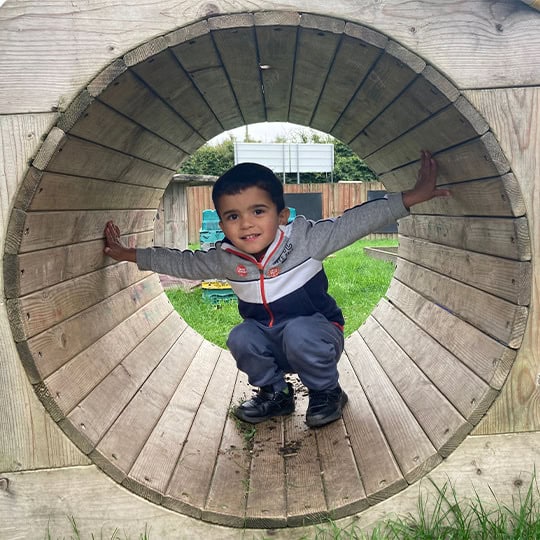 1. Happy child playing inside wooden tunnel at Thrive Childcare, outdoor play area, fostering fun and active learning for children.
