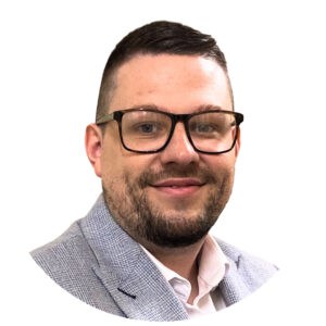 Bright professional portrait of a smiling man wearing glasses and a grey checked blazer, suitable for Thrive Childcare website, highlighting friendly, professional childcare services and staff.
