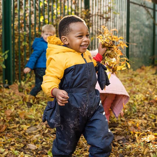 Colourful young children playing outdoors in autumn leaves at Thrive Childcare, showcasing a safe, nurturing environment for early childhood development.