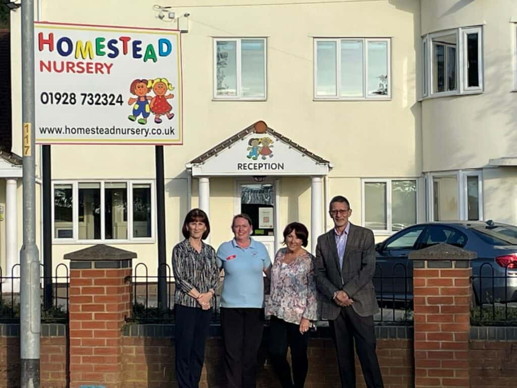 Children and staff outside Homestead Nursery, a welcoming childcare centre in a bright, two-storey building with colourful signs and a reception area, highlighting professional childcare services in a friendly environment.
