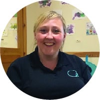 A cheerful childcare professional smiling in a colourful nursery environment, highlighting quality early childhood education and nurturing care at Thrive Childcare.
