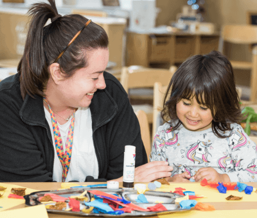Bright female childcare assistant engaging with a young girl in creative arts and crafts at Thrive Childcare centre in the UK.