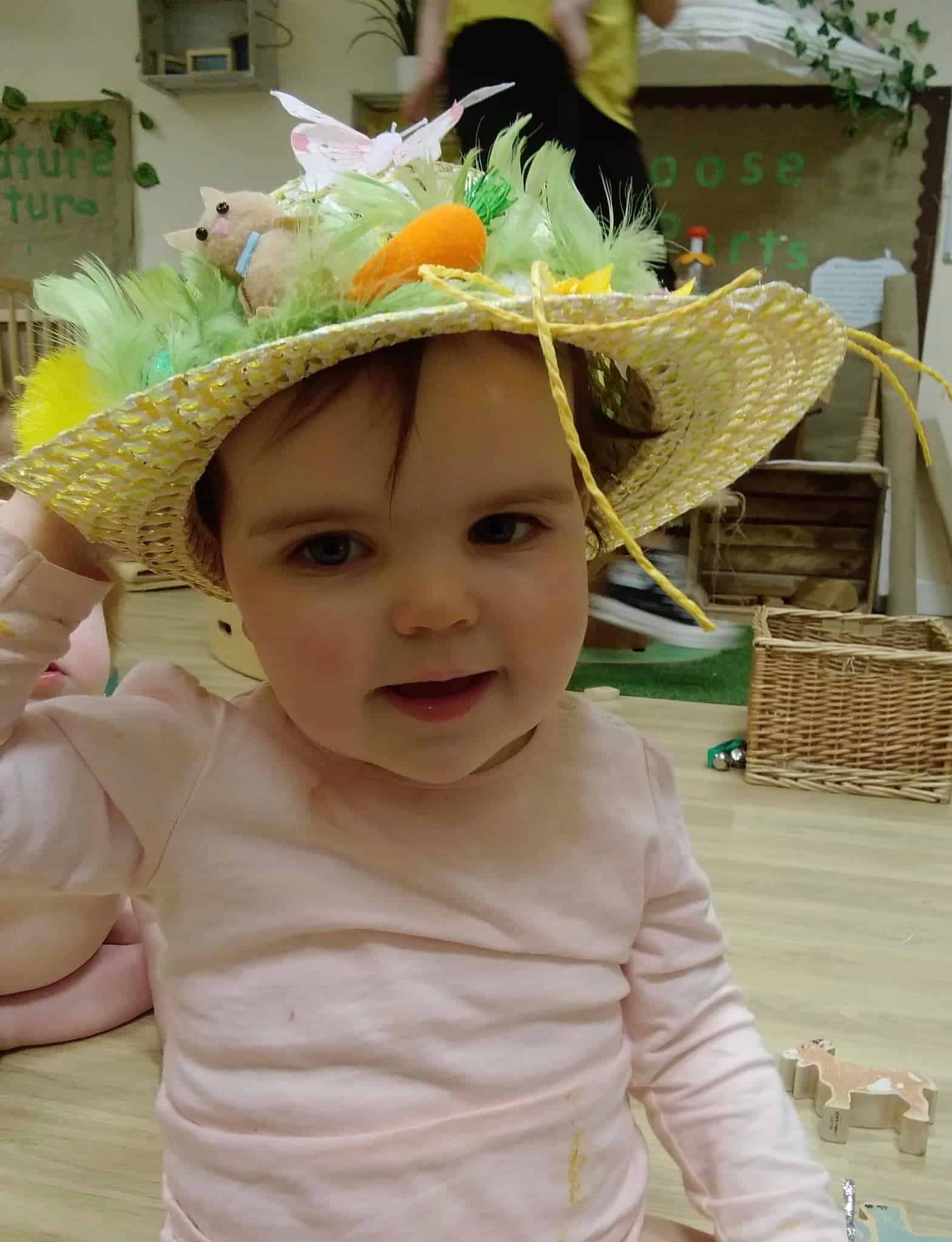 Colourful Easter hat with decorations including a small felt bunny, carrot, and feathers, worn by a young child in a childcare setting, celebrating spring and festive arts and crafts activities.