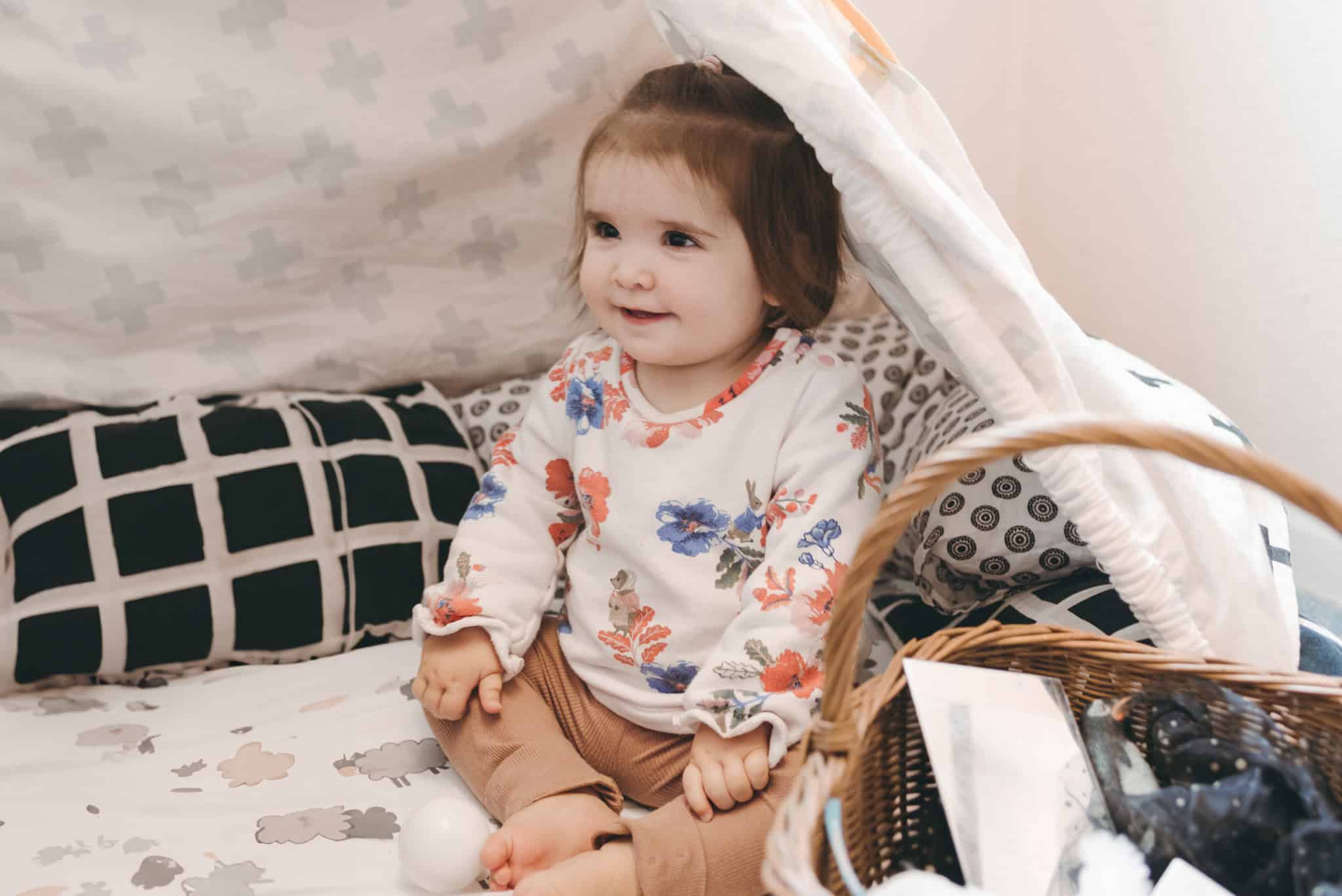 Bright smiling toddler girl enjoying playtime at Thrive Childcare, surrounded by soft bedding and toys, reflecting a nurturing environment for early childhood development and learning.