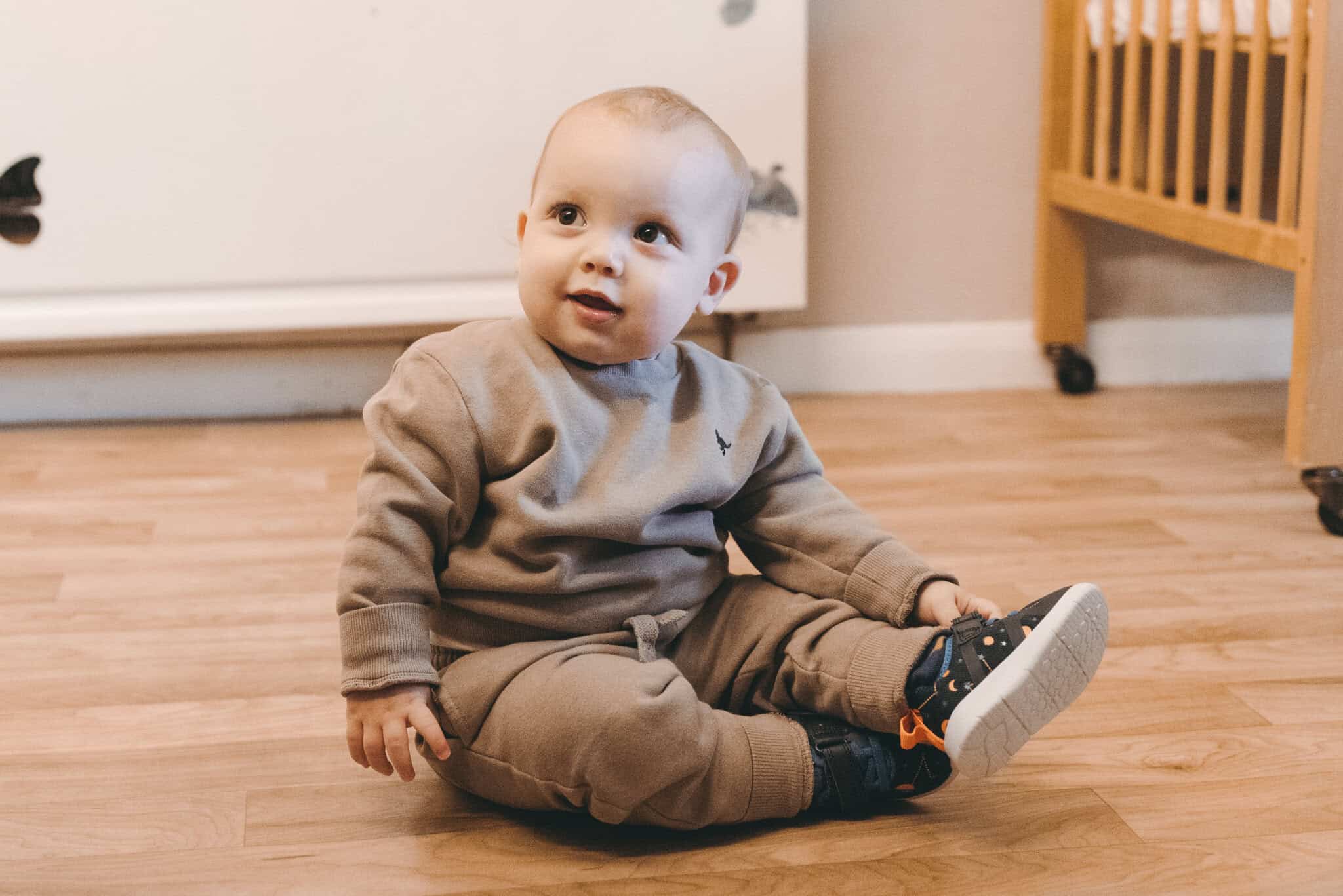 1. Adorable baby sitting on a wooden floor at Thrive Childcare, promoting early childhood education and child development services in a warm, safe environment.