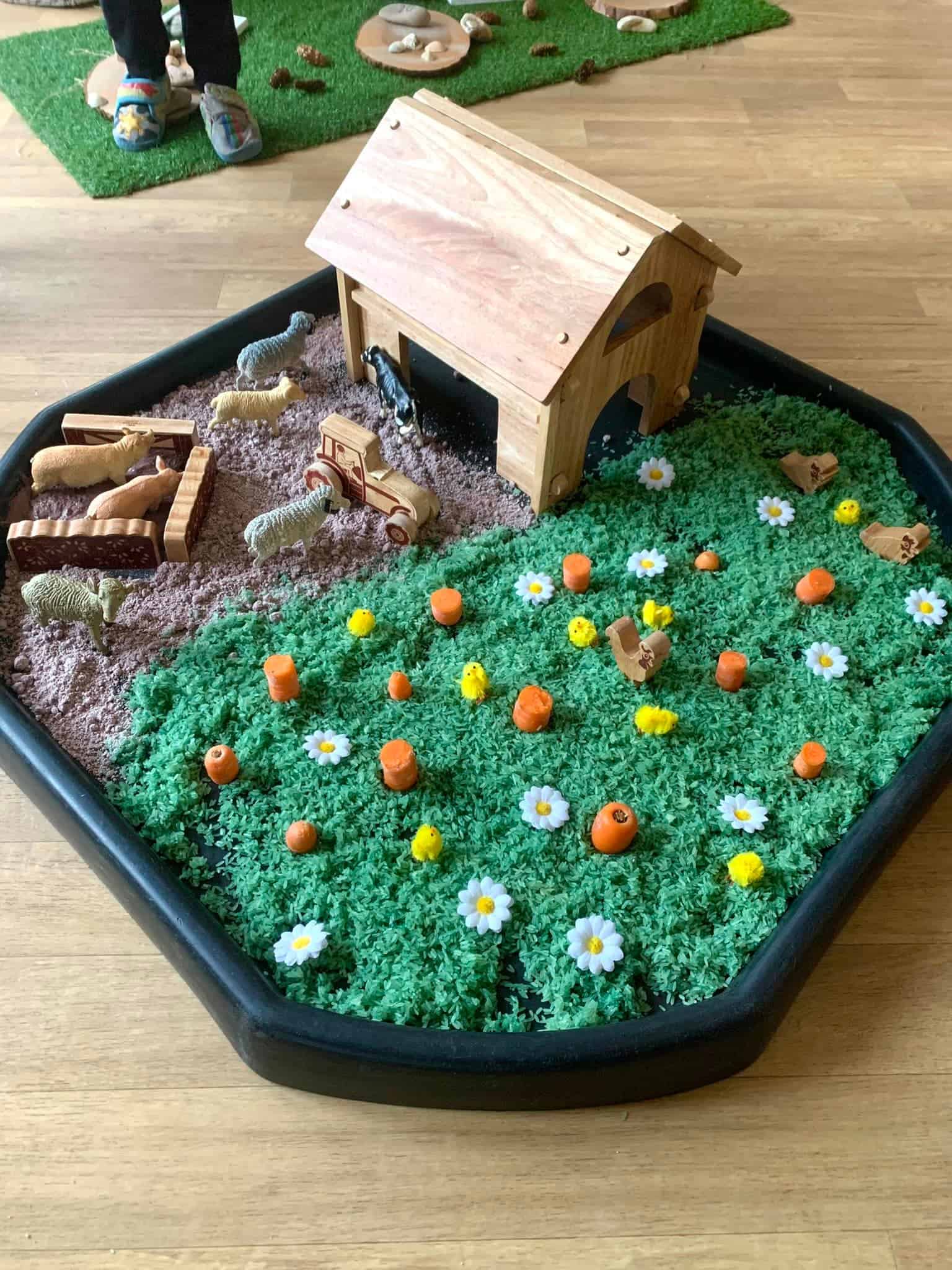 Brightly coloured educational farm-themed sensory play area with toy animals, miniature farm equipment, flowers, and green grass, ideal for early childhood learning and development at Thrive Childcare.
