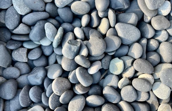 Smooth grey pebbles, natural stone flooring or decoration, close-up of polished stones with varying sizes, textures, and shades, perfect for outdoor or indoor design elements.