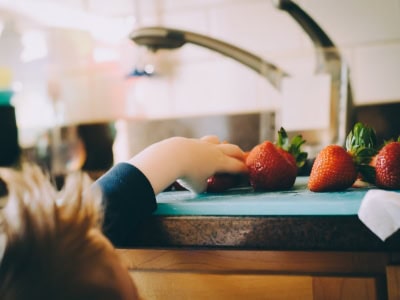 A child’s hand reaching for strawberries on a kitchen counter, highlighting healthy eating and child-friendly learning environments at Thrive Childcare.