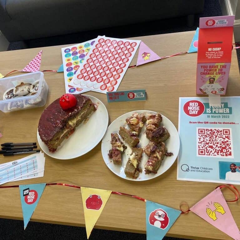 Brightly decorated table at Thrive Childcare for Red Nose Day featuring cakes, charity stickers, donation QR codes, and colourful banners promoting fun, community, and charity engagement for children and families.