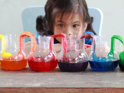 Vibrant child doing a fun science experiment with colourful liquids in small glass bowls at Thrive Childcare.