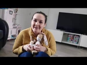 A woman smiling at the camera holding a plush rabbit toy in a bright, modern childcare or playroom setting.