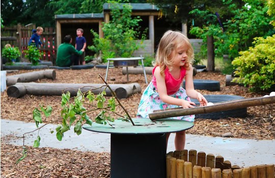 A young girl playing outdoors in a colourful childcare garden at Thrive Childcare, engaging with natural play elements and exploring nature for early childhood development.