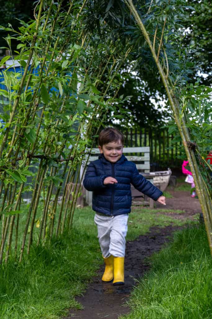Young boy playing outdoors in a lush garden at Thrive Childcare, enjoying nature and outdoor activities with safe, engaging play areas for early childhood development.