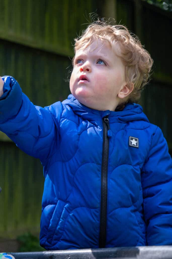 Bright young child in a blue jacket exploring outdoors at Thrive Childcare, fostering curiosity and discovery in a safe, nurturing environment.
