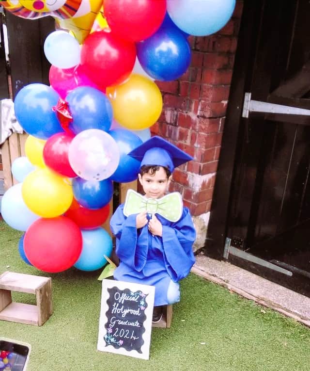 Bright young boy in blue graduation gown and cap celebrating at Thrive Childcare with colourful balloons and a chalkboard sign, highlighting early childhood education and childcare graduation event.
