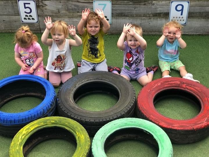 Bright preschool children playing with colourful tyres in outdoor childcare area at Thrive Childcare, promoting fun and active early childhood development.