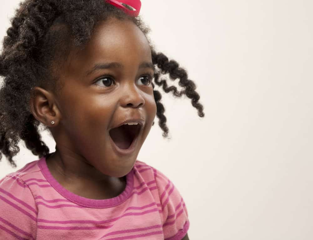 Vibrant African-American girl with curly hair and pink striped shirt expressing joy, highlighting Thrive Childcare's nurturing environment for early childhood development and child happiness.