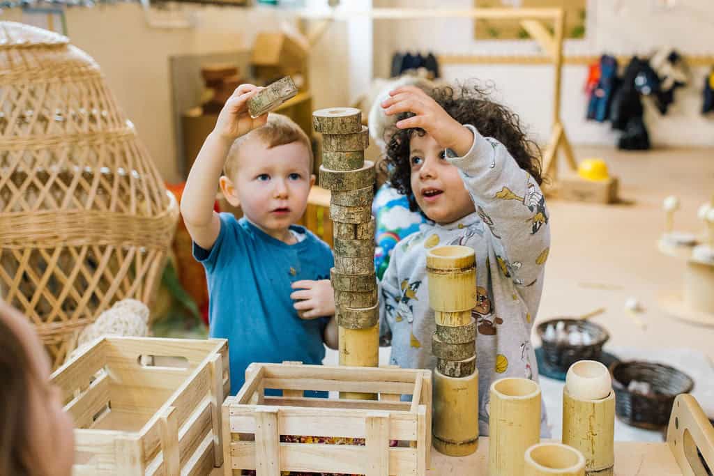 1. two young children playing with wooden stacking blocks in a colourful childcare setting, fostering creativity and fine motor skills, at Thrive Childcare.