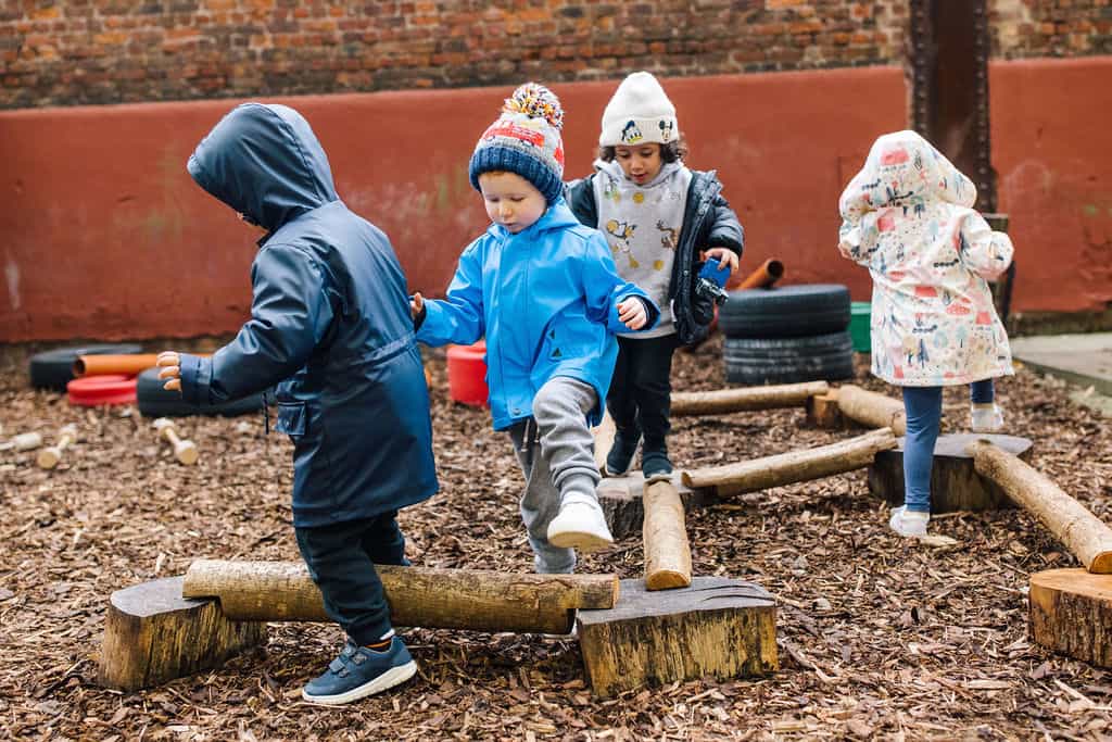 Children playing on outdoor balance beams at Thrive Childcare, promoting physical activity and outdoor learning for early childhood development.