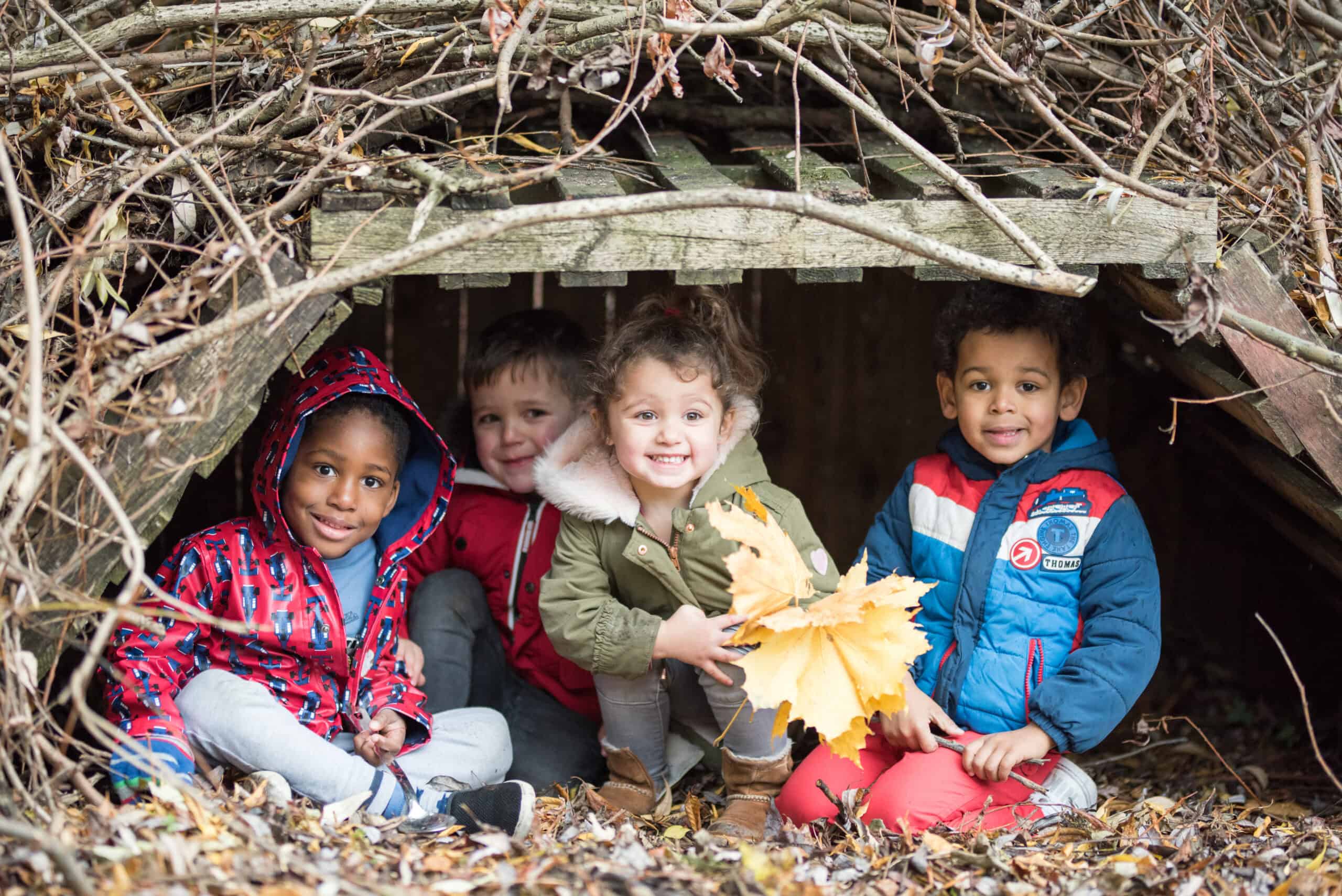 Bright and happy children playing and exploring outdoors in a natural woodland school environment, fostering early childhood development and outdoor learning at Thrive Childcare.