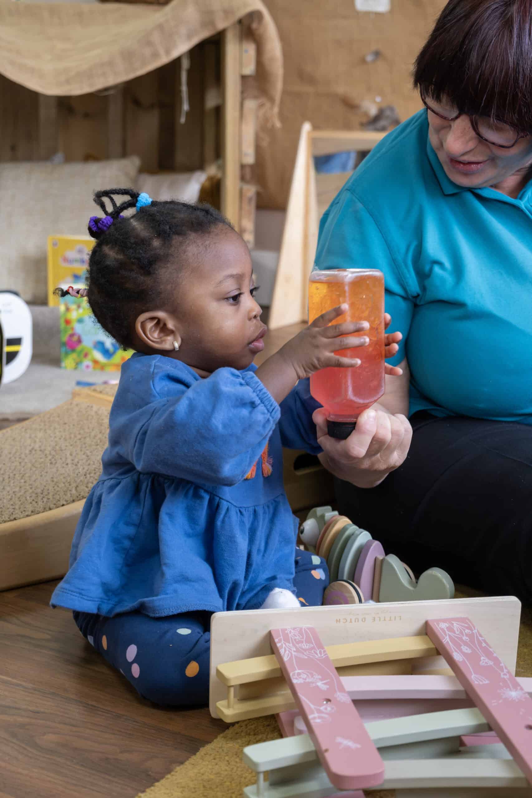 1. Young African-American girl in blue dress exploring sensory play with a caregiver in a colourful childcare setting at Thrive Childcare.