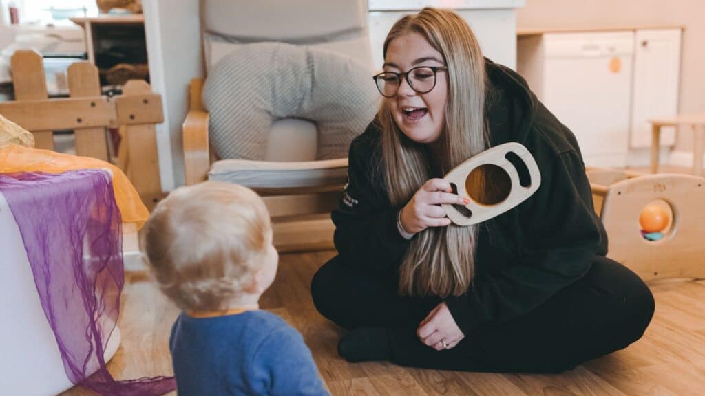 Engaging childcare professional using a wooden teaching aid with a young child in a warm, educational environment at Thrive Childcare.