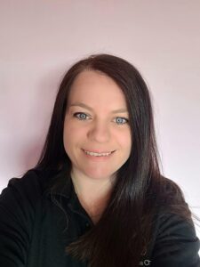 Bright smiling child care professional with dark brown hair and blue eyes, promoting a nurturing environment at Thrive Childcare, dedicated to early childhood education and development.