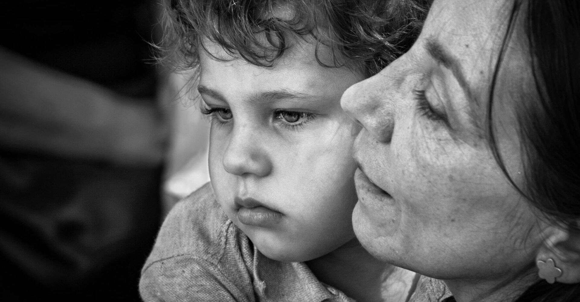 Close-up of a young boy and an adult woman sharing a tender moment, emphasizing family connection, care, and emotional bonds in black and white.