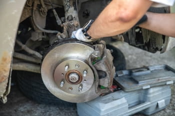 Technician inspecting car brake disc and caliper during repair.