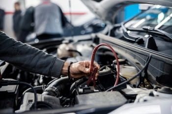 Technician inspecting car battery in a vehicle engine bay.