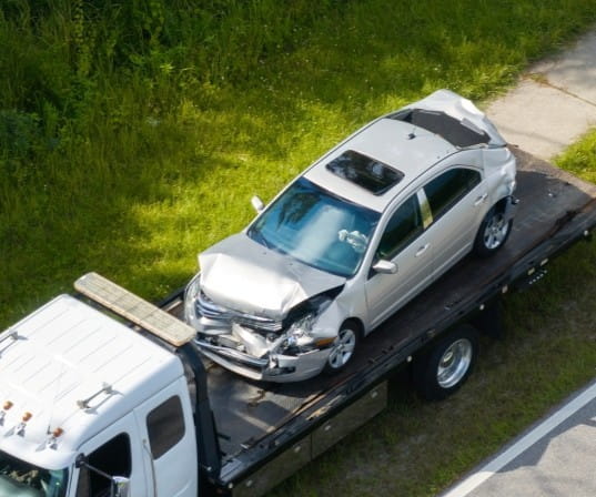 Silver car with front-end damage on tow truck after accident.