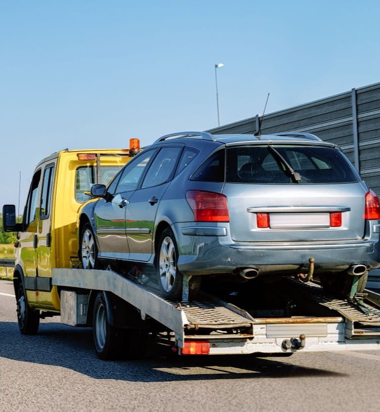 Tow truck transporting a silver car on highway for roadside assistance.