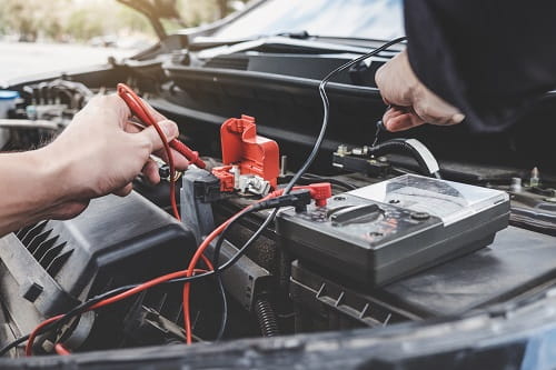 Technician testing car battery with multimeter under the hood.