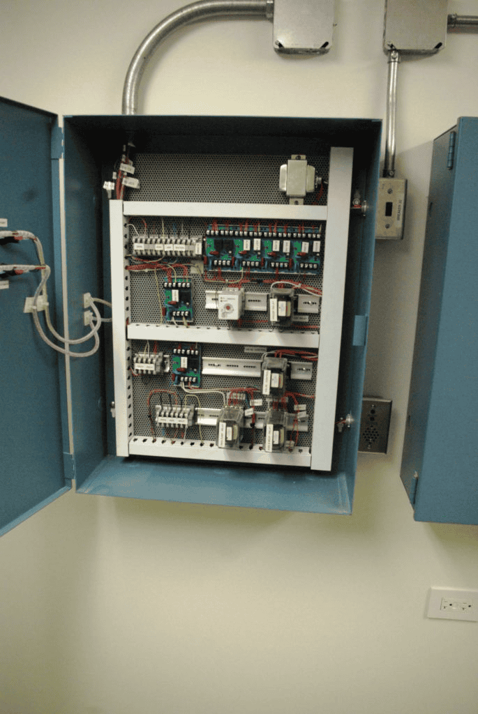 An Open Electrical Control Panel With Various Wiring, Switches, And Components Inside A Blue Metal Box Mounted On A Wall.
