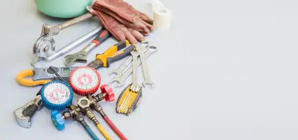 A set of HVAC tools including wrenches, gauges, pliers, gloves, and a utility knife arranged on a flat surface.