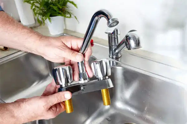 Person holding a chrome kitchen faucet above a stainless steel sink.