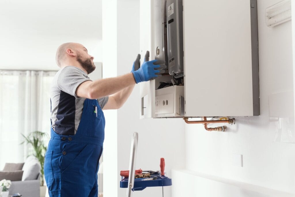 A technician in blue overalls and gloves diligently provides heating services, working on a wall-mounted boiler with tools neatly arranged on a cart nearby in the bright room.